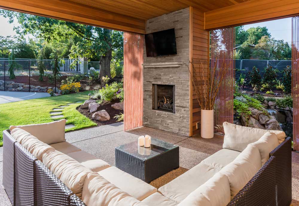 beautifuly designed outdoor entertaining space with a full height fireplace, tv, wooden covered ceiling, slidable curtains, and cushioned outdoor furniture.
